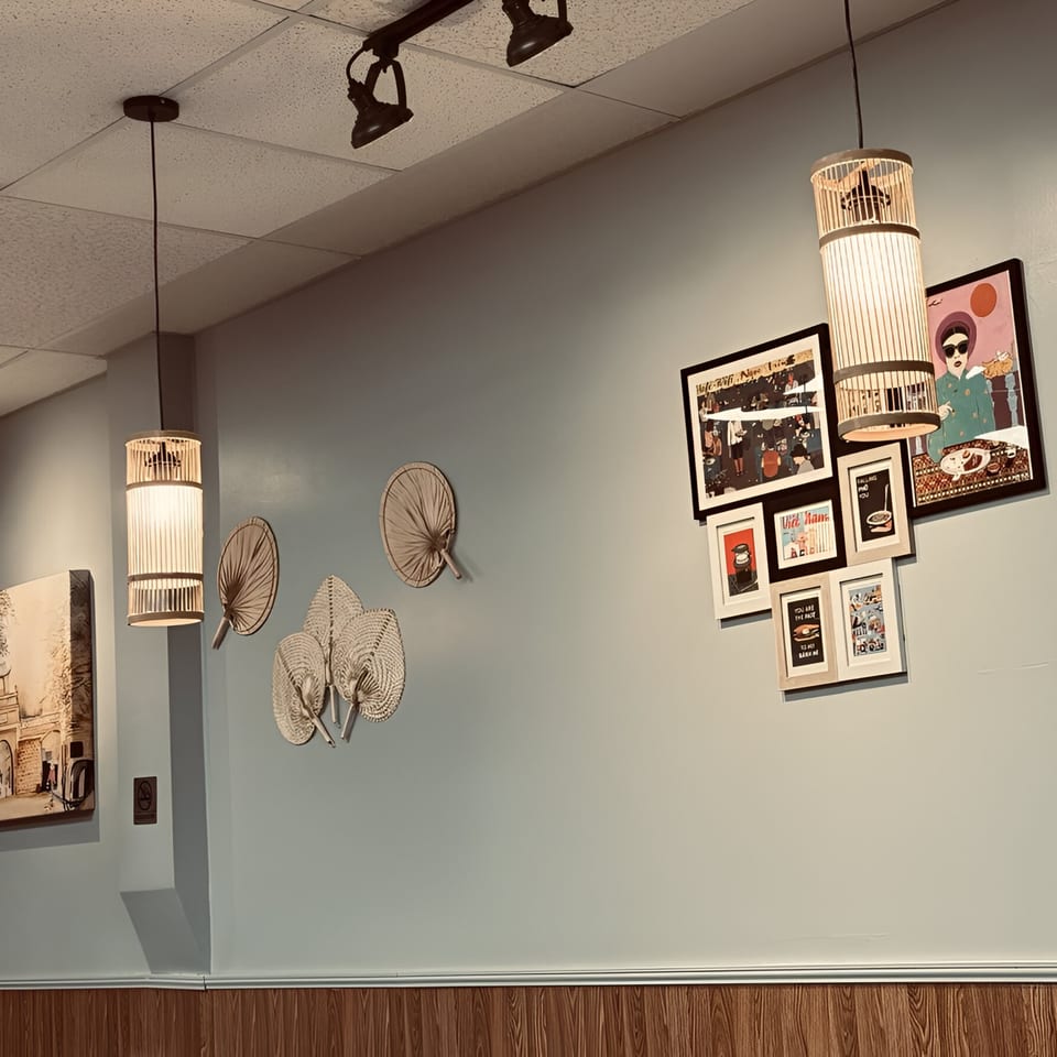 Light blue wall with framed art, decorative fans, and bamboo pendant lights in Pho Delight.