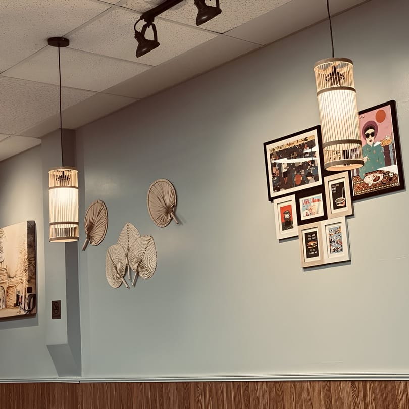 Light blue wall with framed art, decorative fans, and bamboo pendant lights in Pho Delight.