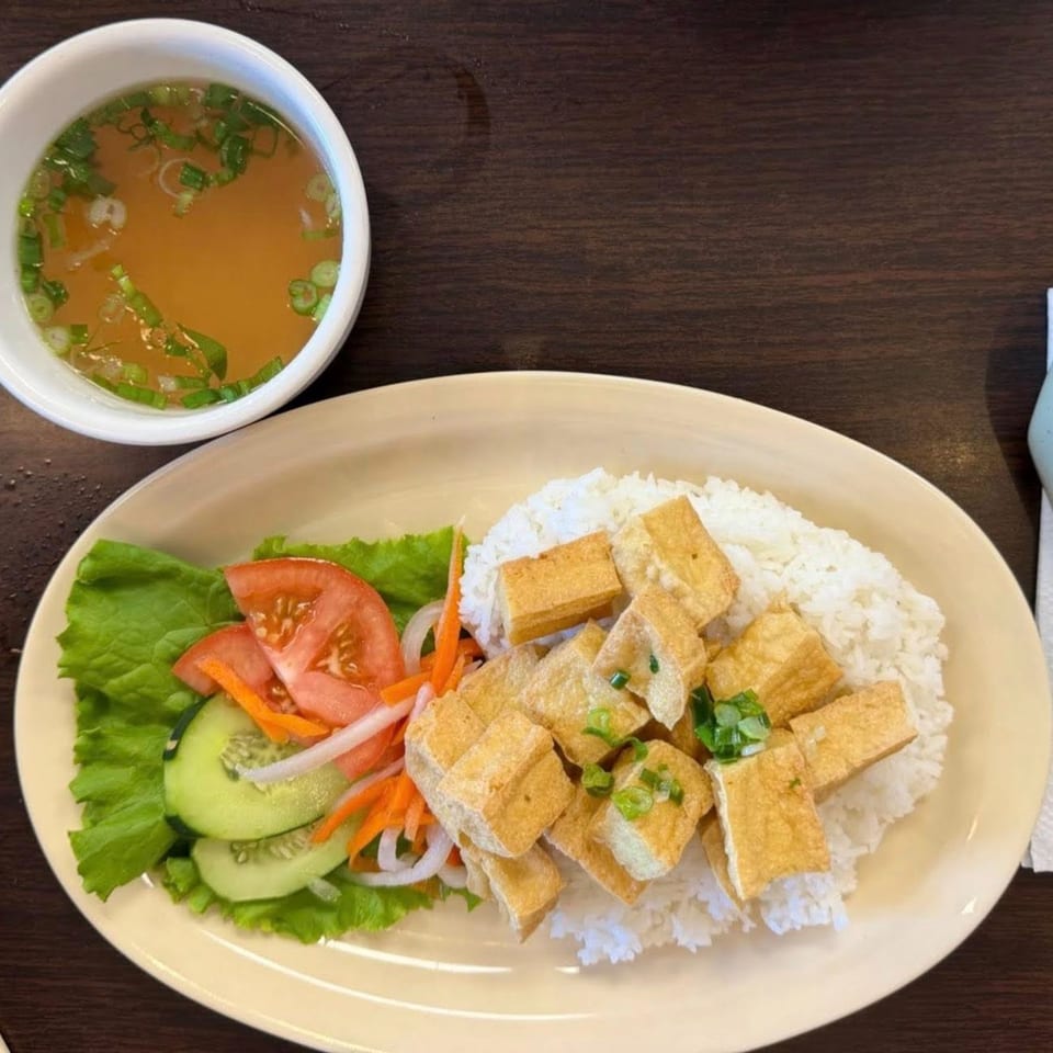 Vietnamese fried tofu and rice with a side salad and a bowl of broth on a wooden table.