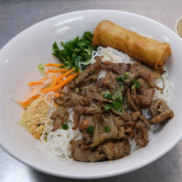 Vietnamese vermicelli bowl with grilled pork, egg roll, vegetables, and crushed peanuts.