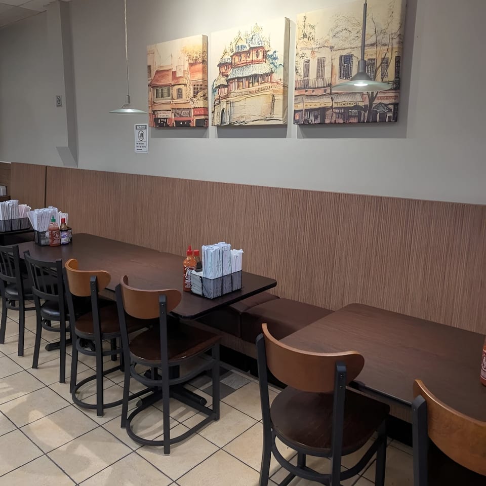 Empty dining area at Pho Delight with dark wood tables, chairs, and wall art depicting buildings.