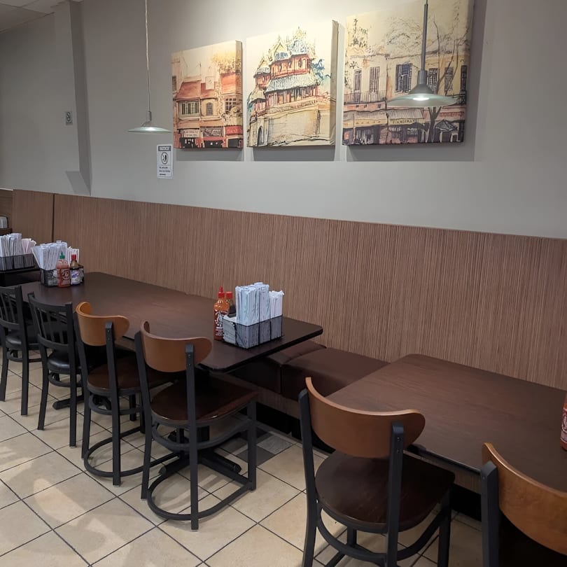 Empty dining area at Pho Delight with dark wood tables, chairs, and wall art depicting buildings.