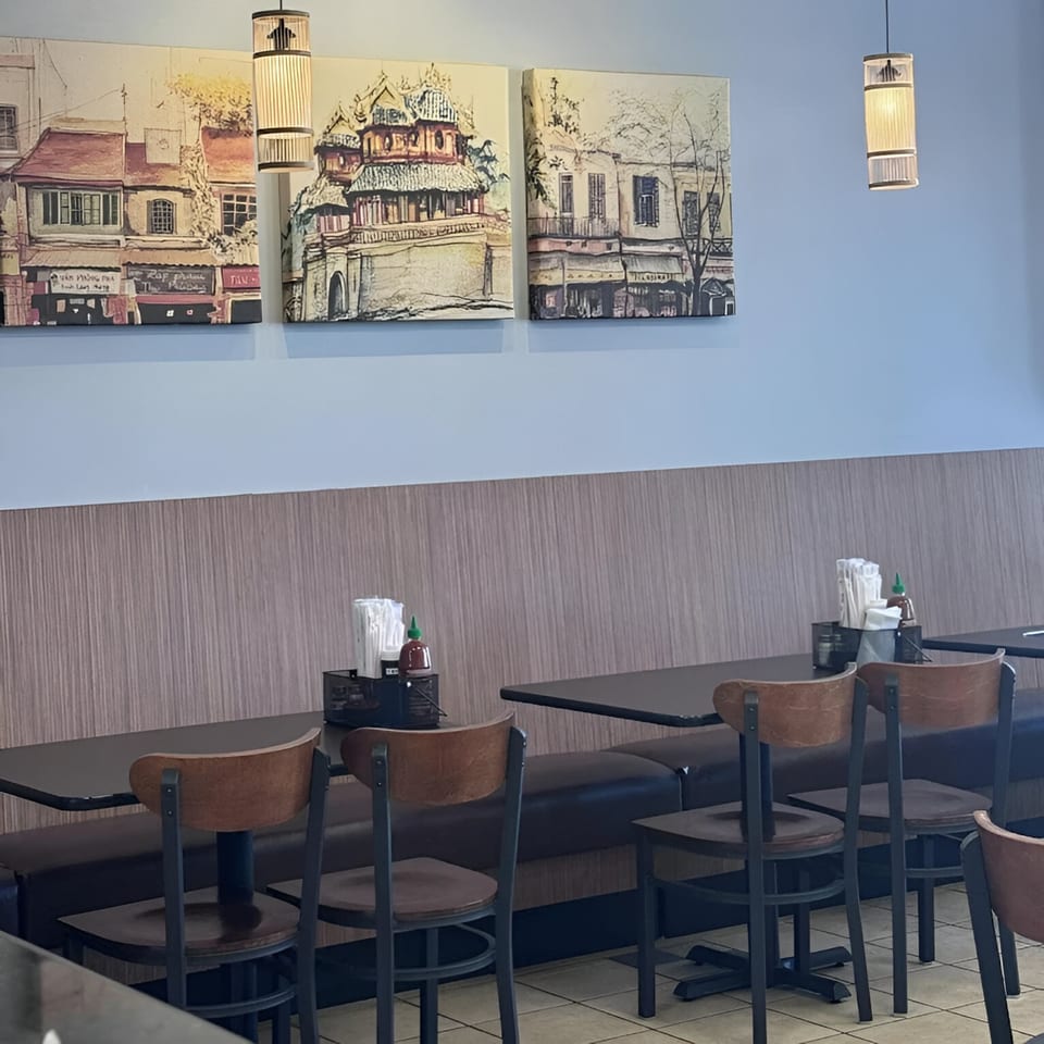 Interior of Pho Delight restaurant with empty tables, chairs, and Vietnamese-themed artwork on the wall.