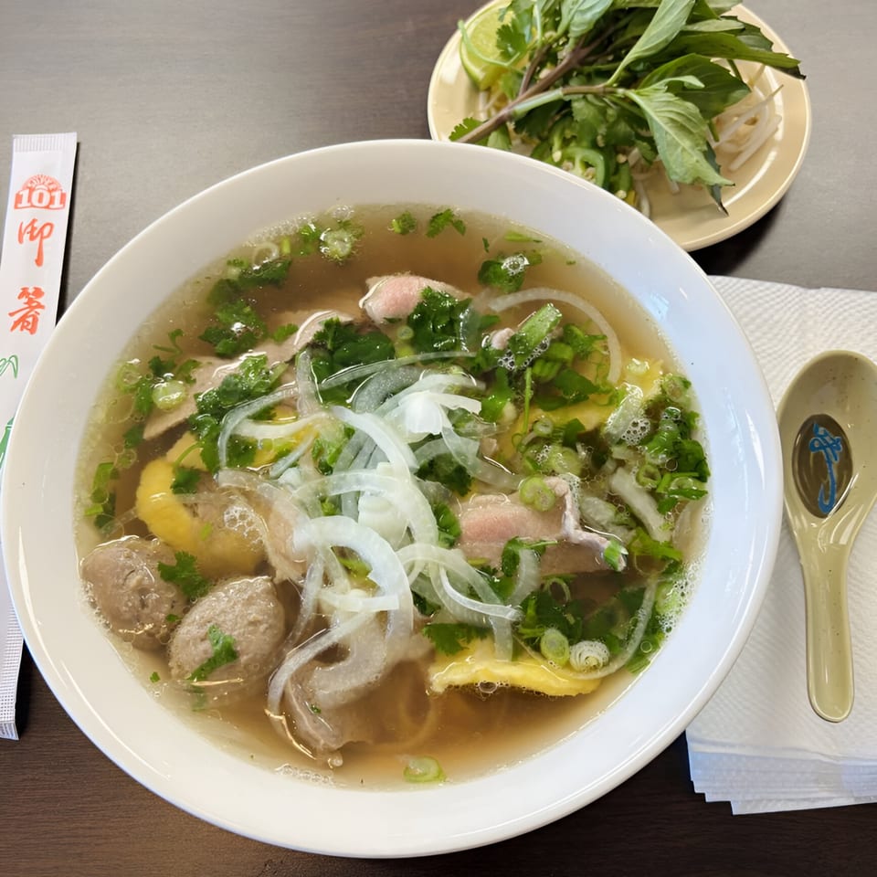 A bowl of Pho Delight's Vietnamese pho with meat, noodles, and fresh herbs.