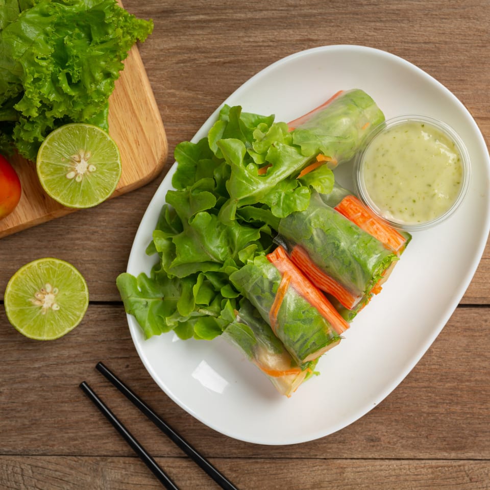 Fresh Vietnamese spring rolls with crab sticks, lettuce, and a side of green dipping sauce.